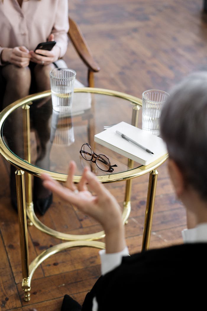 services-05 Two adults engaged in a therapy session, seated at a glass table with notebooks and water glasses.